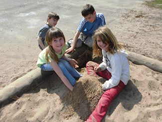 Vier Kinder sitzen im Sandkasten und buddeln die Füße ein